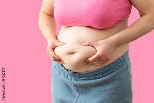 Close up of a obese young woman checking her fats against a pink background © INAOX