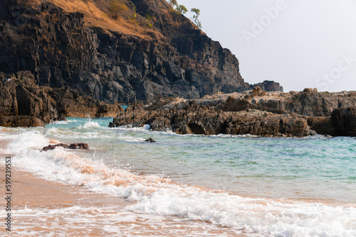 Sea waves crashing on a rock in the sea as seen from Kakolem Beach in Goa, India. Water waves crashing on the rock in the middle of sea. Nature relaxing background. Rock in the middle of blue water. 