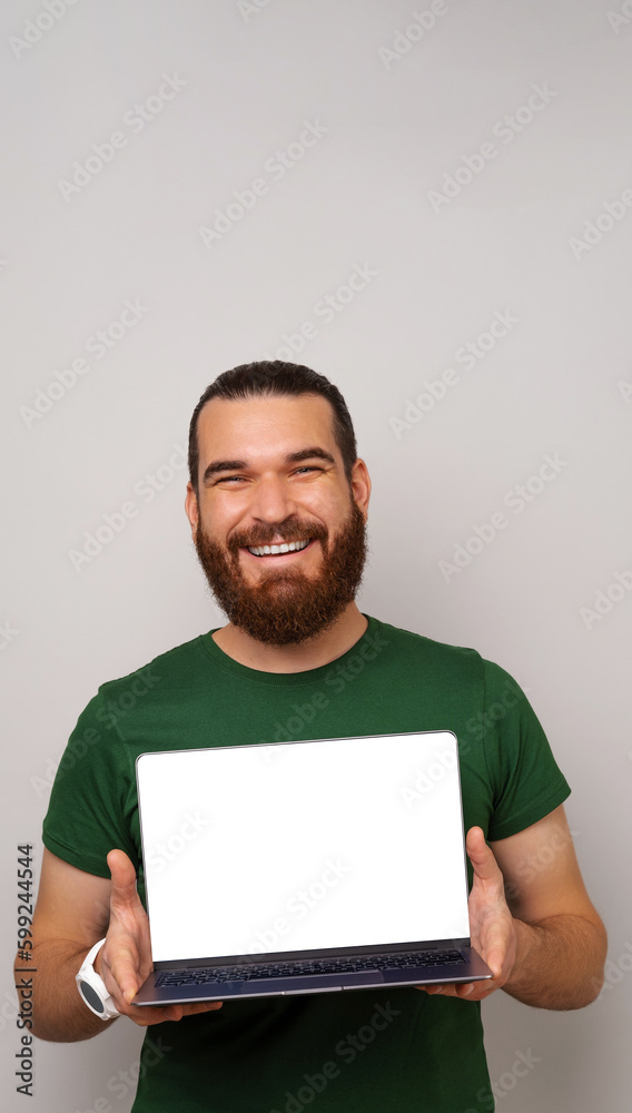 Vertical shot of a bearded man is holding a laptop and showing blank screen with copy space. Vertical shot of a bearded man is holding a laptop and showing blank screen with copy space.