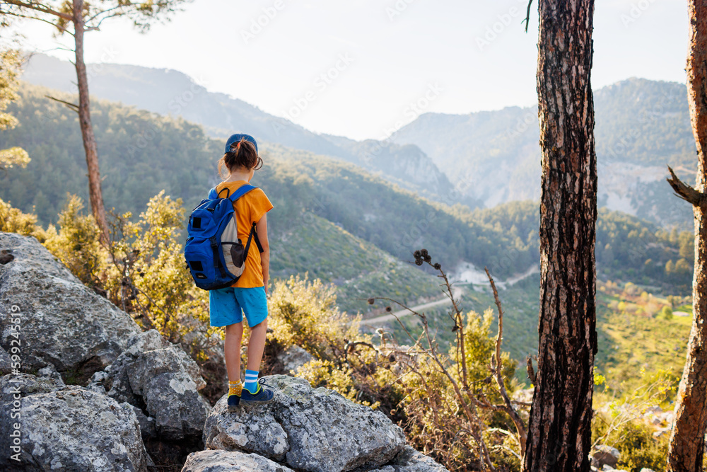 Naklejka premium Traveling child. a tourist with a backpack stands on a mountain path looks at the mountains. hiking and active healthy lifestyle.