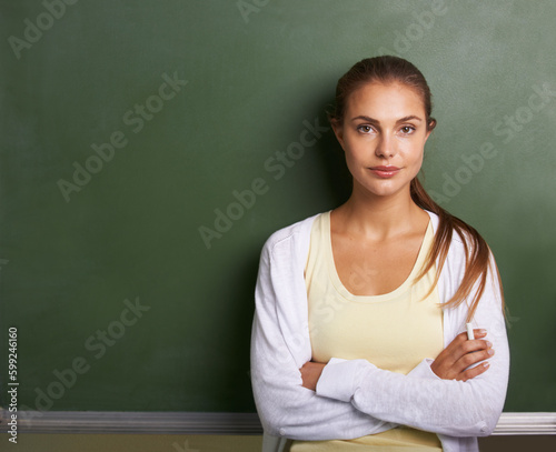 Confidence in the classroom. A lovely young teacher standing in front of a blackboard with her arms folded - copyspace. © Tylan E/peopleimages.com