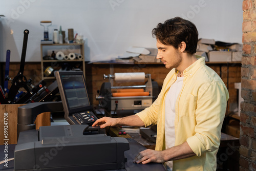 young man in yellow shirt using professional printer near monitor.