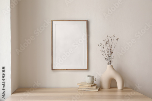 Neutral home still life. Decorative boho interior. Vase with bouquet of dry plants, grass on wooden table. Blank picture frame mockup hanging on wall. White cup of coffee or tea,books. Artistic poster