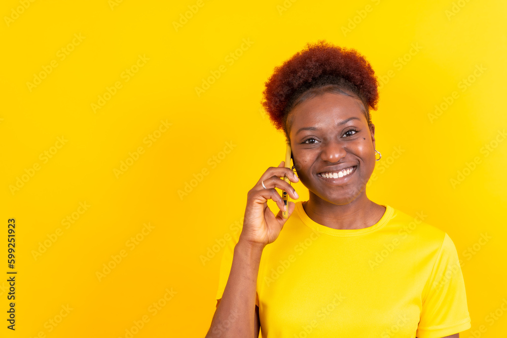 Young african american woman isolated on a yellow background smiling with the mobile phone, study session Young african american woman isolated on a yellow background smiling with the mobile phone, study session