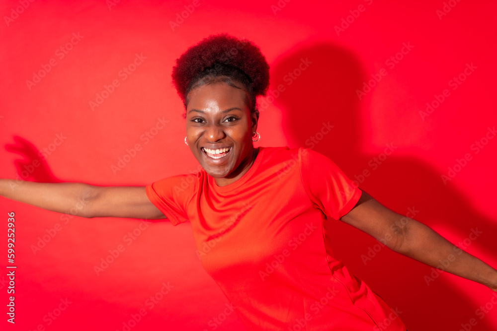 Young african american woman isolated on a red background smiling and dancing, studio shoot Young african american woman isolated on a red background smiling and dancing, studio shoot