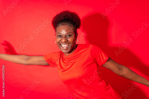 Young african american woman isolated on a red background smiling and dancing, studio shoot