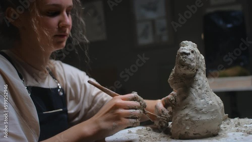 European blonde girl sculptor creates sculpture, statue for interior, bozzetto. The woman has her own local business, a freelancer. The female uses the tools of a sculptor, stecca for clay. photo