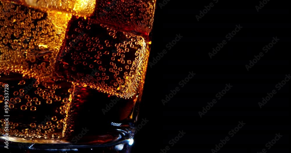 Pouring Cola with ice cubes close-up. Cola with Ice and bubbles in glass. Coke Soda closeup. Food background. Rotate glass of Cola fizzy drink over brown background. Slow motion 4K UHD video footage