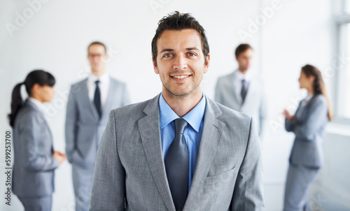He excels at business. Portrait of a handsome young businessman smiling while his colleagues stand blurred in the background.