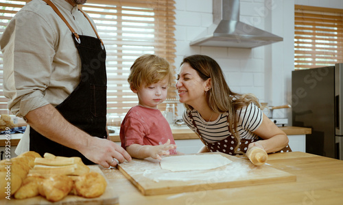 Father and mother teaching baby son kneading dough on kitchen counter at home. Parents and boy kid enjoy and fun indoors activity cooking together.