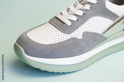 Sneakers for everyday use on a pale green background. Sneaker toe with suede and white leather with holes for air circulation. Summer footwear for sports, recreation, travel.