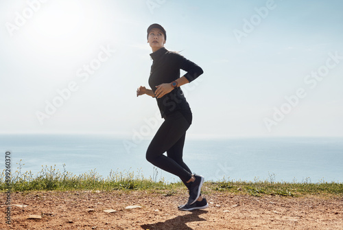 This is second nature to her. a determined young woman going for a jog on her own with a view of the ocean in the background.