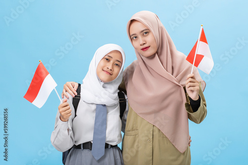 Muslim woman student with a teacher celebrate indonesia independence day waving flag of indonesian isolated over blue background photo