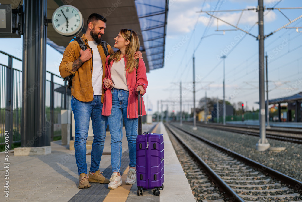 Happy couple is standing at railway station and waiting for arrival of their train.