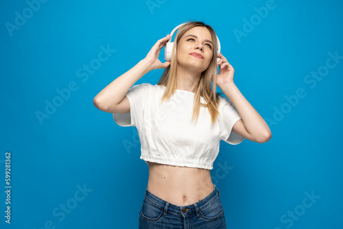 Young blonde woman with headphones listening music .Music teenager girl dancing against isolated blue background.