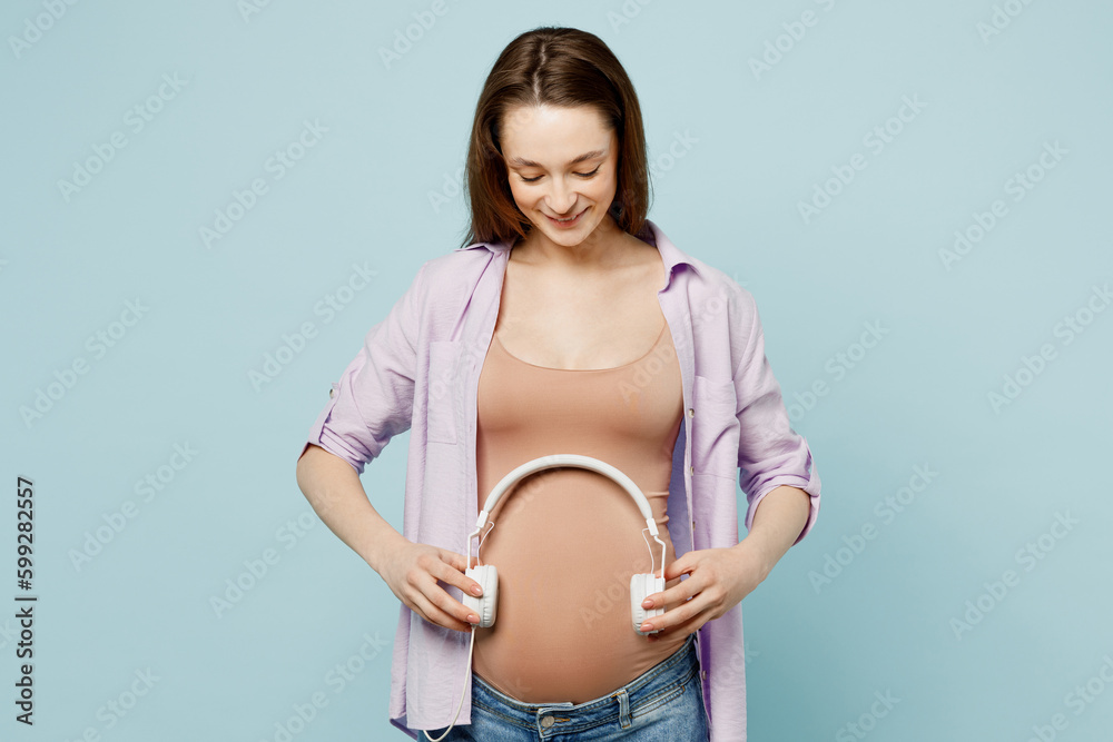 Young fun relaxed pregnant future mom woman with tummy wearing casual  clothes put headphones on belly for baby to listen to music isolated on  plain pastel blue background. Maternity pregnancy concept. Stock