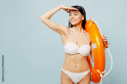 Young sexy woman wear swimsuit hold in hand lifeguard inflatable ring look aside far away near hotel pool isolated on plain pastel light blue cyan background. Summer vacation sea rest sun tan concept.