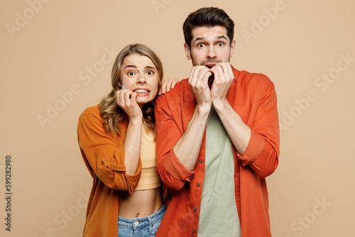 Young shocked scared fearful couple two friends family man woman wear casual clothes looking camera biting nails fingers together isolated on pastel plain light beige color background studio portrait. photo