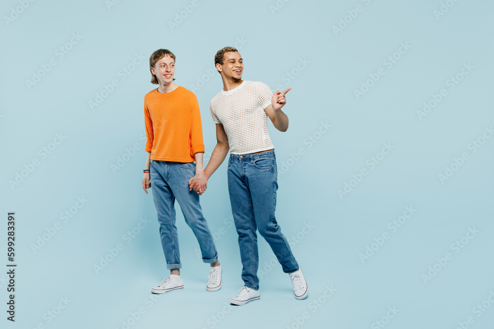 Obraz premium Full body sideways young couple two gay men wear casual clothes together walk go hold hands point aside isolated on pastel plain blue color background studio. Pride day june month love LGBTQ concept.