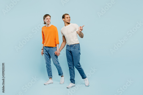 Full body sideways young couple two gay men wear casual clothes together walk go hold hands point aside isolated on pastel plain blue color background studio. Pride day june month love LGBTQ concept. © ViDi Studio