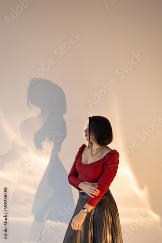Woman wearing a skirt and red top, with a short haircut, against a white wall © Tetiana Romaniuk