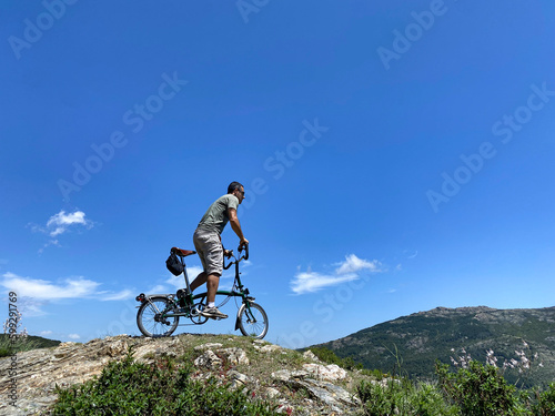 Un Uomo sulla sua bici pedala sopra una roccia  isolata su sfondo cielo azzurro