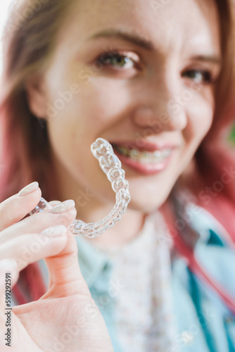 Dental care.Smiling girl with braces on her teeth holds aligners in her hands and shows the difference between them