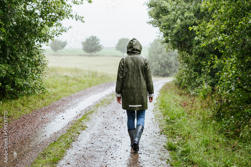 Rear view of woman in green raincoat walking in rain photo