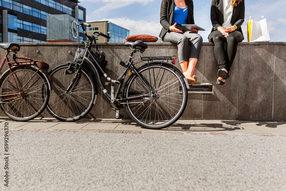 Low section of two women with bicycles sitting on wall Low section of two women with bicycles sitting on wall