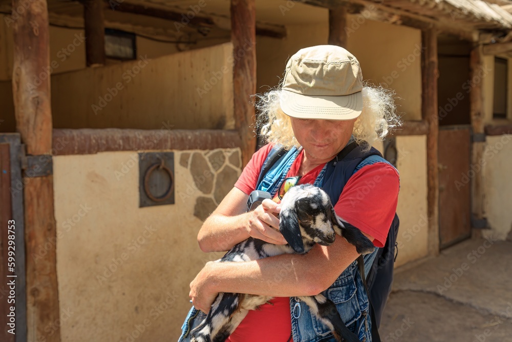 cowboy is interacting with a billy, petting and stroking him with affectionate care. Little goat is cute and friendly, and farmer caresses him tenderly, showing his love for this small cub of nature. cowboy is interacting with a billy, petting and stroking him with affectionate care. Little goat is cute and friendly, and farmer caresses him tenderly, showing his love for this small cub of nature.