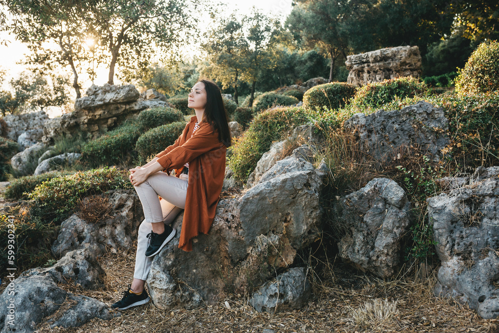 A beautiful young girl is sitting alone on a stone in an olive grove and enjoying the weather, thinking A beautiful young girl is sitting alone on a stone in an olive grove and enjoying the weather, thinking