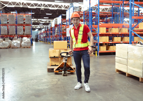 Young man pulling hand pallet truck loading package boxes stacked in shipping warehouse. Asian worker moving merchandise from storage shelf by hand lift pallet jack. Delivery goods, cargo transport.