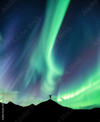 Aurora borealis glowing over silhouette hiker standing on the mountain in the night sky