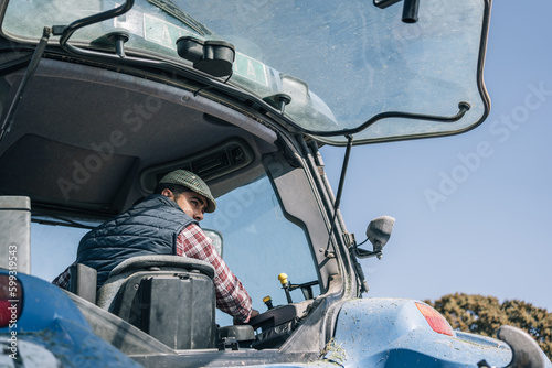 Rear exterior image of a young farmer in a beret maneuvering his tractor in reverse.