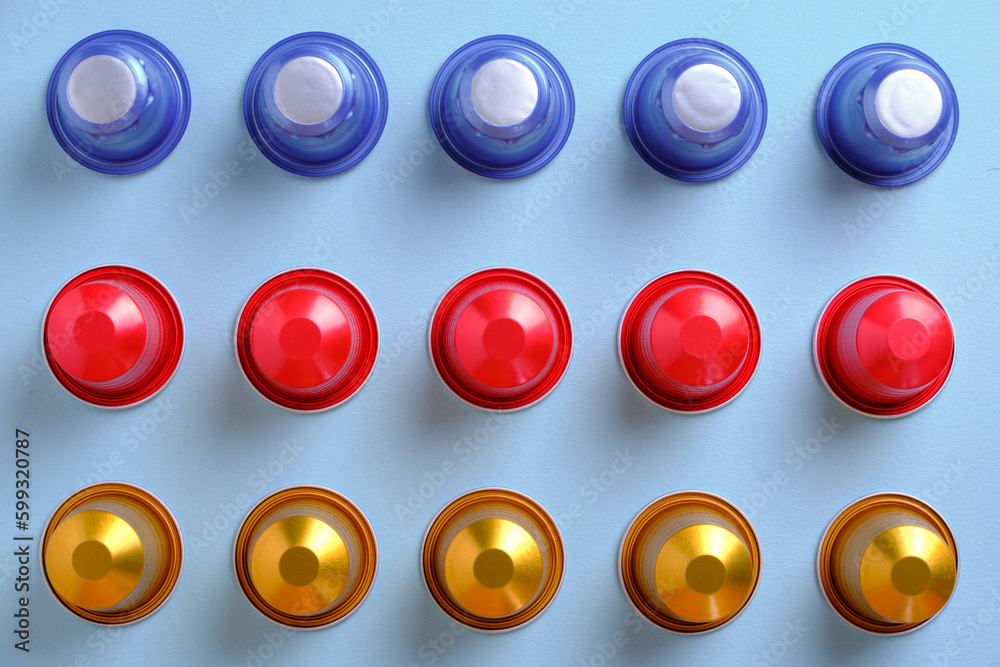 Multi-coloured coffee pods in a grid against a plain background. Top down view.