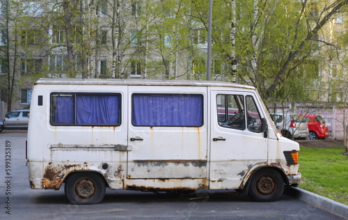 An old rusty white minibus is parked in the courtyard of a residential building, Belysheva Street, St. Petersburg, Russia, May 2023