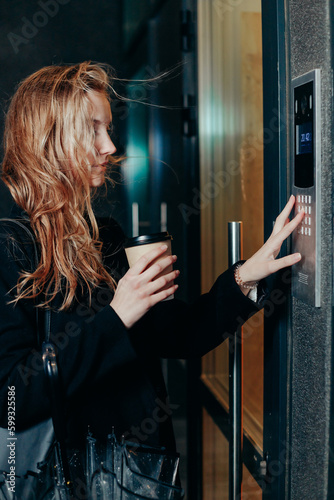 Woman dialing a number on the on video intercom at entrance of apartment building in the night © vladdeep