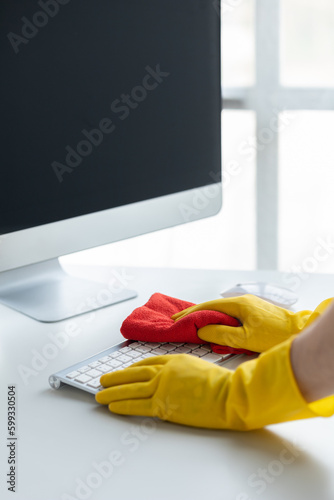 Person cleaning room, cleaning worker is using cloth to wipe computer keyboard in company office room. Cleaning staff. Concept of cleanliness in the organization.