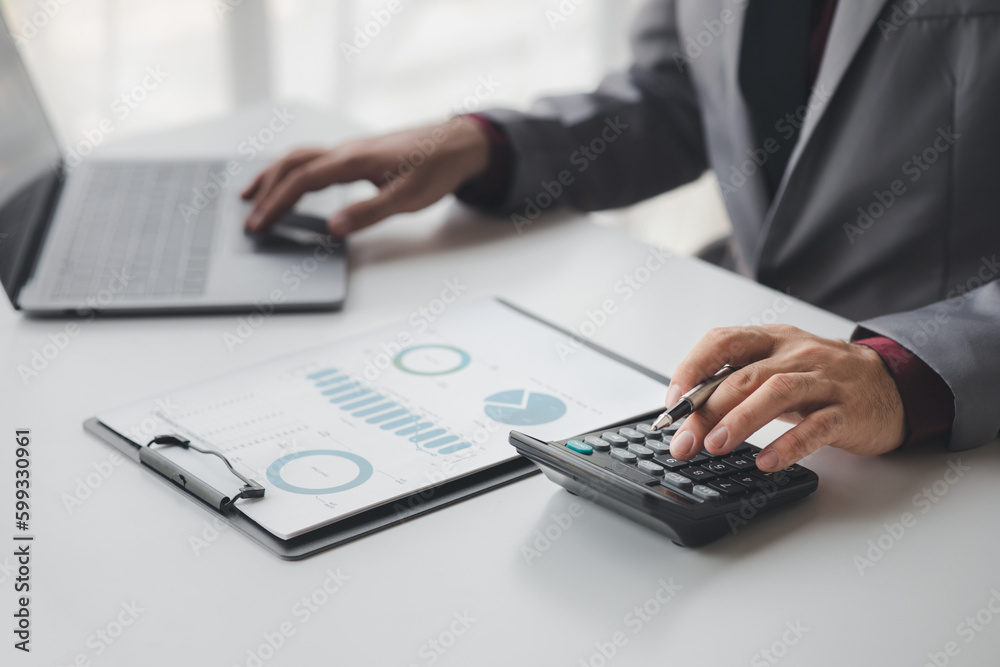 Businessman using a calculator to calculate numbers on a company's financial documents, she is analyzing historical financial data to plan how to grow the company. Financial concept. Businessman using a calculator to calculate numbers on a company's financial documents, she is analyzing historical financial data to plan how to grow the company. Financial concept.