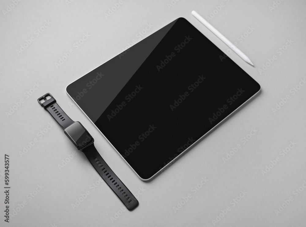Digital tablet with blank black screen, fitness bracelet and stylus pen on gray paper background