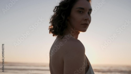 Young beautiful girl in dress smiling, spinning, walking on the beach at sunset.