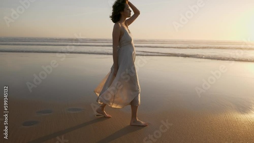 Beautiful young woman walking at sunset on the ocean shore. Romantic scene at sunset.