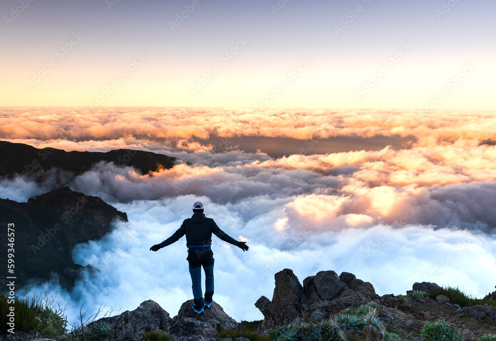 Adventure hiker standing on mountain top above clouds at sunset or sunrise in Madeira, Portugal