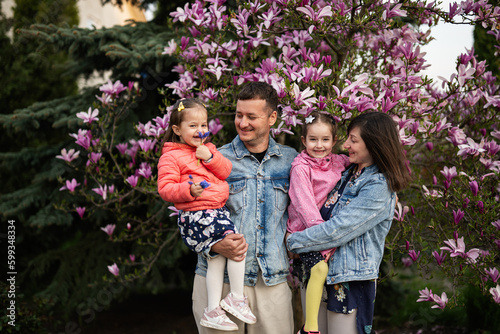 Happy family with two daughters enjoying nice spring day near magnolia blooming tree.