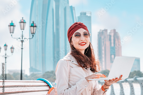 Canvas Print From the comfort of her laptop, a freelancer or student indian girl immerses herself in the vibrant and dynamic atmosphere of downtown Abu Dhabi, fueled by the energy of the bustling city