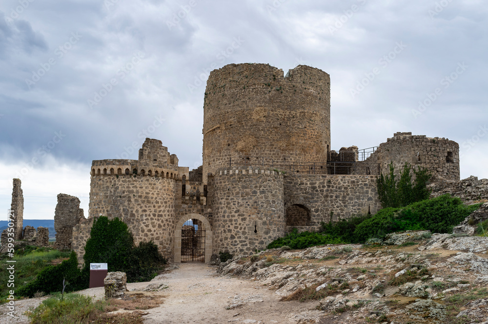 imagen del castillo de Moya, castillo de piedra entre naturaleza, suelo de rocas y tierra con hierbas verdes y el cielo nublado 