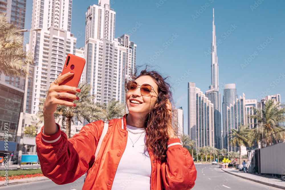 Fototapeta premium Tourist happy girl taking photos for her travel blog, in Dubai downtown district against background of the Burj Khalifa highest skyscraper