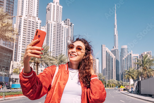 Fototapeta Tourist happy girl taking photos for her travel blog, in Dubai downtown district