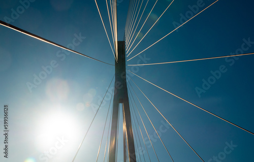 Suspension bridge support cables against a blue sky and sunbeam reflections. Buildings and structures in Norway. Bottom view