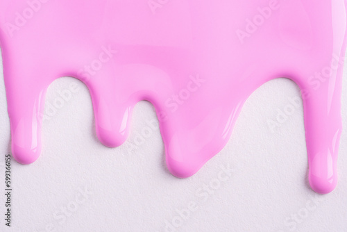 Pink liquid drops of paint color flow down on white canvas. Abstract art. Light pink paint dripping on the white wall with copy space..